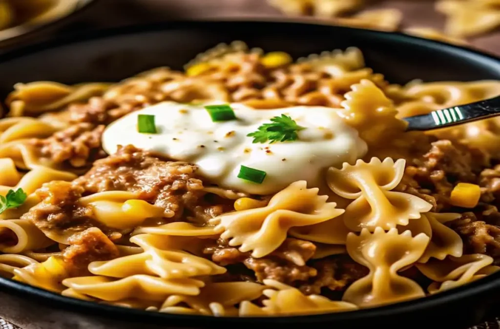 Close-up of a creamy ranch beef bowtie pasta skillet with sweet corn, garnished with fresh parsley and a dollop of seasoned sauce, served in a black pan.Creamy Ranch Beef Bowtie Skillet with Sweet Corn Magic
